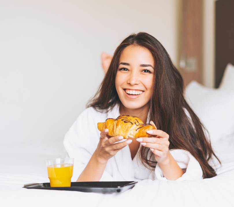 Brünette Frau mit Croissant im Bett